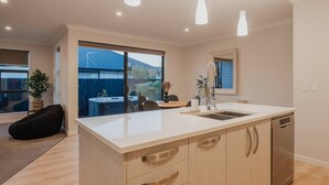 Une cuisine moderne dotée d’un grand îlot central, de luminaires suspendus et offrant une vue sur le jardin.