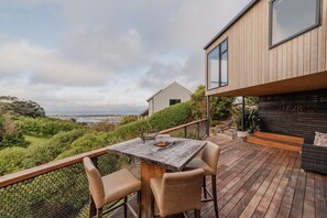 Une terrasse en bois avec une table et des chaises, offrant une vue panoramique sur un paysage pittoresque composé de collines et d’une étendue d’eau.