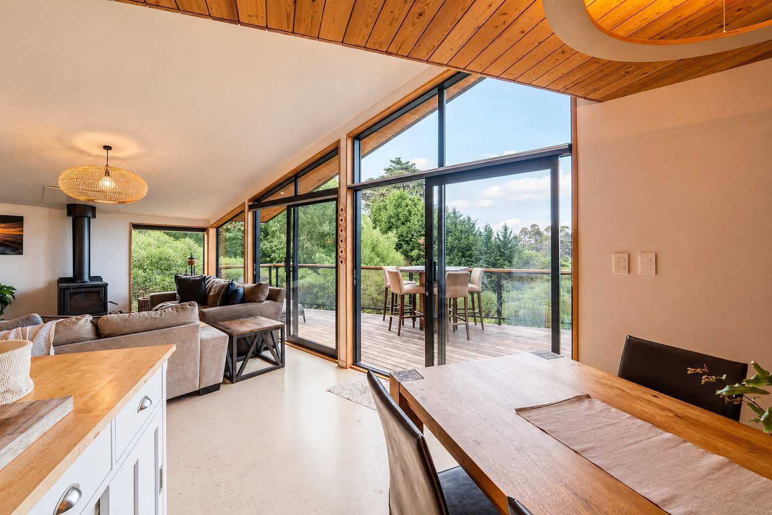 Ein modernes Interieur mit Holzboden, großen Schiebeglasüren zu einer Außenterrasse, einem eingebauten Kamin und einem Essbereich.
