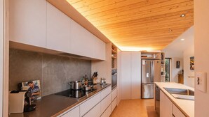 A modern kitchen with a wooden ceiling, stainless steel appliances, and a long countertop. - Ocean Views | 3BR Home with Hot Tub & Parking (Christchurch)