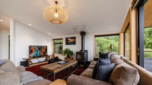A modern living room with a sofa, a coffee table, a TV, and a fireplace. - Ocean Views | 3BR Home with Hot Tub & Parking (Christchurch)