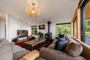 A modern living room with a sofa, a coffee table, a TV, and a fireplace. - Ocean Views | 3BR Home with Hot Tub & Parking (Christchurch)