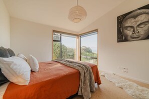 Une chambre avec un grand lit, une vue sur l’extérieur et une statue de Bouddha accrochée au mur.
