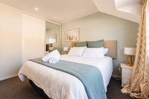 A hotel room with a bed, a bedside table, a lamp, a mirror, and a painting on the wall.