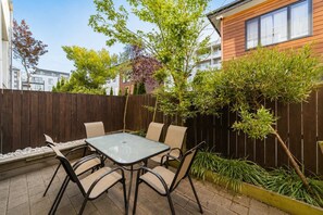 An outdoor patio with a glass table and four chairs, surrounded by a wooden fence and various plants. - Worcester 3BR | Garage | Central Christchurch (Christchurch)