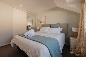 A hotel room with a large bed, a bedside table with a lamp, a mirror, and a framed picture on the wall. - Quaint Worcester Quarters - 3BR Delight (Christchurch)