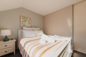Een opgemaakt bed met streepjesbeddengoed, een bedlampje en een ingelijst foto aan de muur.