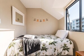 A bedroom with a bed, a window, a wall-mounted mirror, and a string of decorative items. - Worcester 3BR | Garage | Central Christchurch (Christchurch)