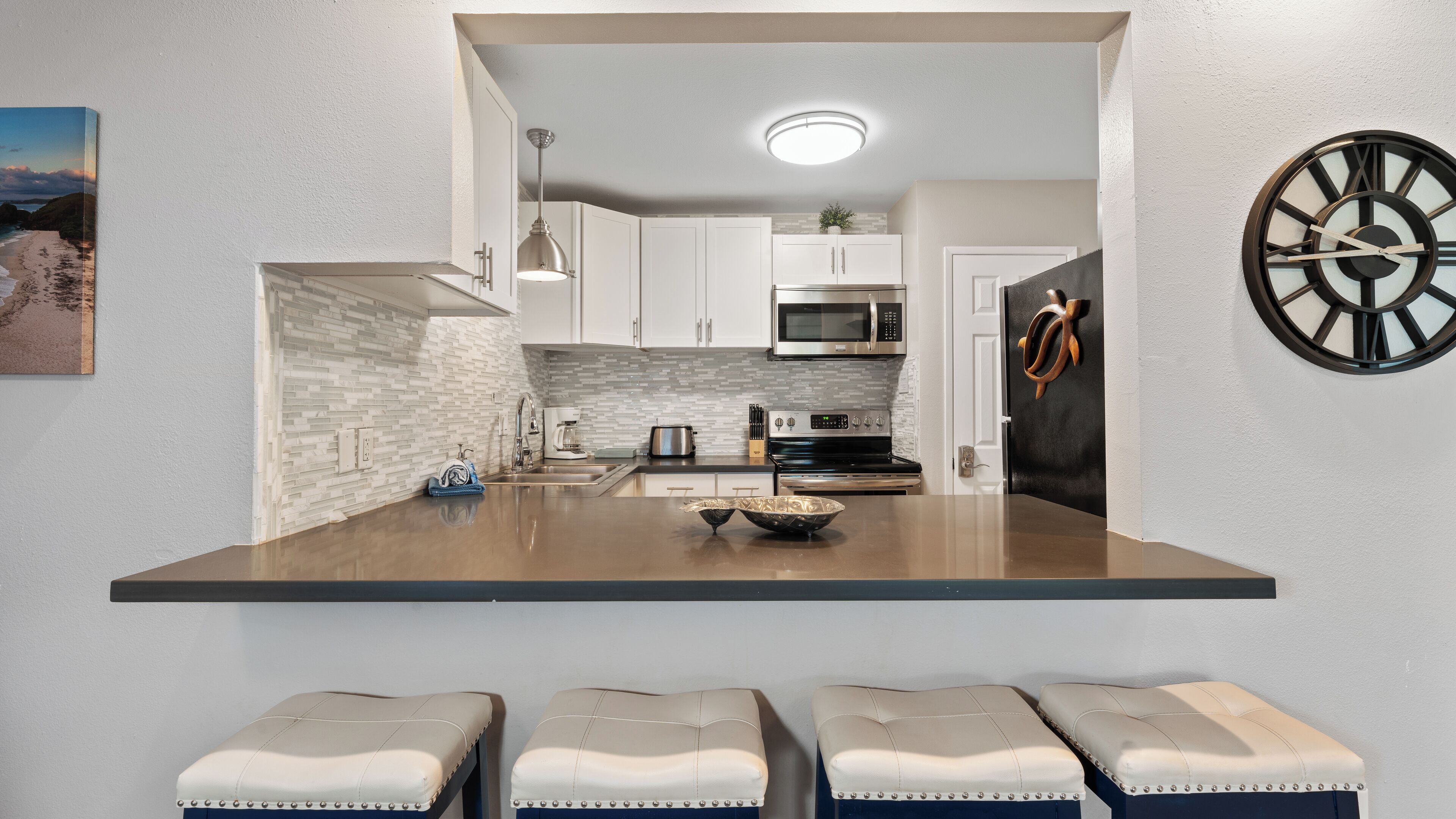 A modern kitchen with white cabinets, a stainless steel range, and a black clock on the wall.
