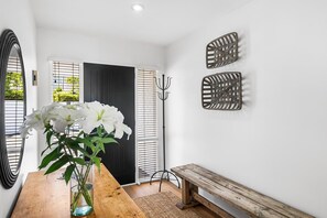 A hallway with a wooden bench, a vase with flowers, a coat rack, and decorative wall art. - KaleidoNook | 3BR + Parking + Private Yard (Christchurch)