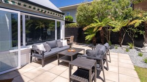 A modern patio with a sofa, two tables, and chairs. - KaleidoNook | 3BR + Parking + Private Yard (Christchurch)