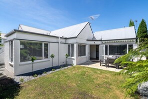 A modern house with a white exterior, large windows, and a patio area with outdoor furniture. - KaleidoNook | 3BR + Parking + Private Yard (Christchurch)
