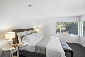 A modern bedroom with a large bed, bedside lamps, a bench, and a window with blinds. - KaleidoNook | 3BR + Parking + Private Yard (Christchurch)
