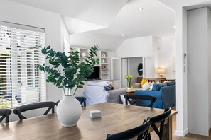 A modern living room with a dining area, featuring a large plant, a sofa set, and a TV. - KaleidoNook | 3BR + Parking + Private Yard (Christchurch)