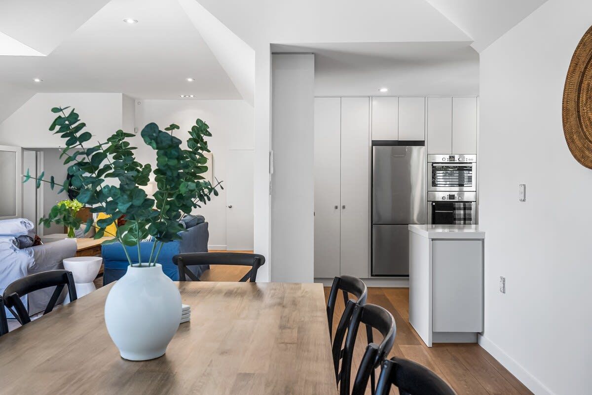 Una cocina moderna con electrodomésticos de acero inoxidable, un comedor con mesa y sillas de madera, y una planta grande en el centro.