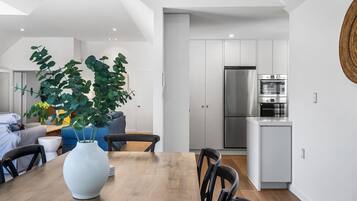 Una cocina moderna con electrodomésticos de acero inoxidable, un comedor con mesa y sillas de madera, y una planta grande en el centro.