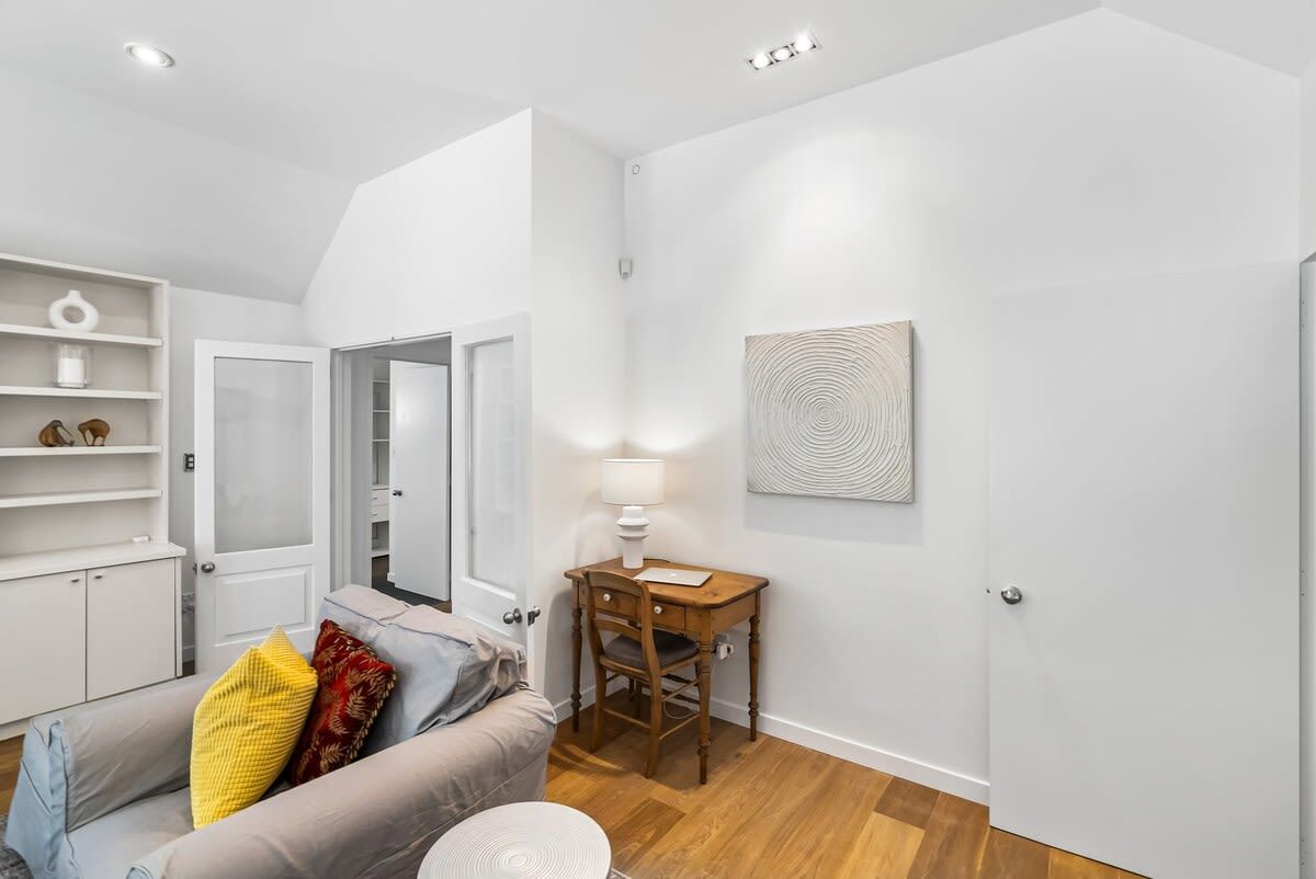 Een moderne woonkamer met een bank, een klein houten tafeltje met een lamp en een witte deur.