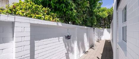 Um caminho estreito ladeado por paredes de tijolos brancos, que leva a um edifício com fachada branca.