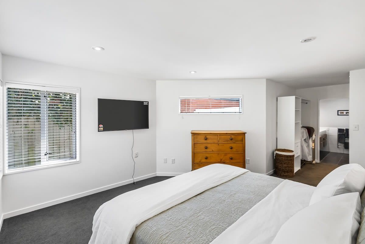 A bedroom with a bed, a dresser, a television, and a window with blinds.