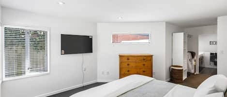 A bedroom with a bed, a dresser, a television, and a window with blinds.