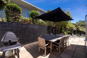 An outdoor patio with a table and chairs, a grill, and an umbrella. - KaleidoNook | 3BR + Parking + Private Yard (Christchurch)