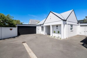 A single-story building with a garage, a small garden, and a clear blue sky. - KaleidoNook | 3BR + Parking + Private Yard (Christchurch)