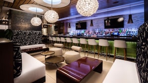 A modern bar area with round tables, bar stools, and hanging crystal chandeliers.