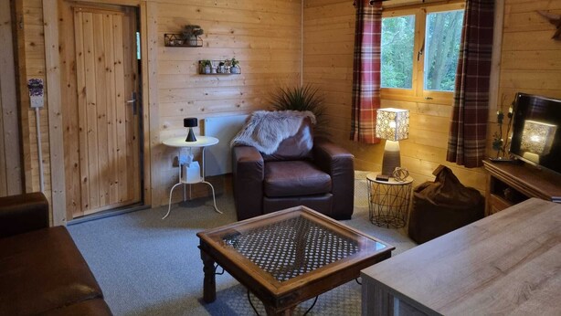 L’intérieur d’un chalet accueillant, avec un plafond en bois, un canapé en cuir, une table basse en verre, une petite table d’appoint et un téléviseur.