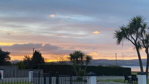 Un espace extérieur clos, agrémenté d’une vue sur le coucher de soleil, avec un plan d’eau, des palmiers et une haie.