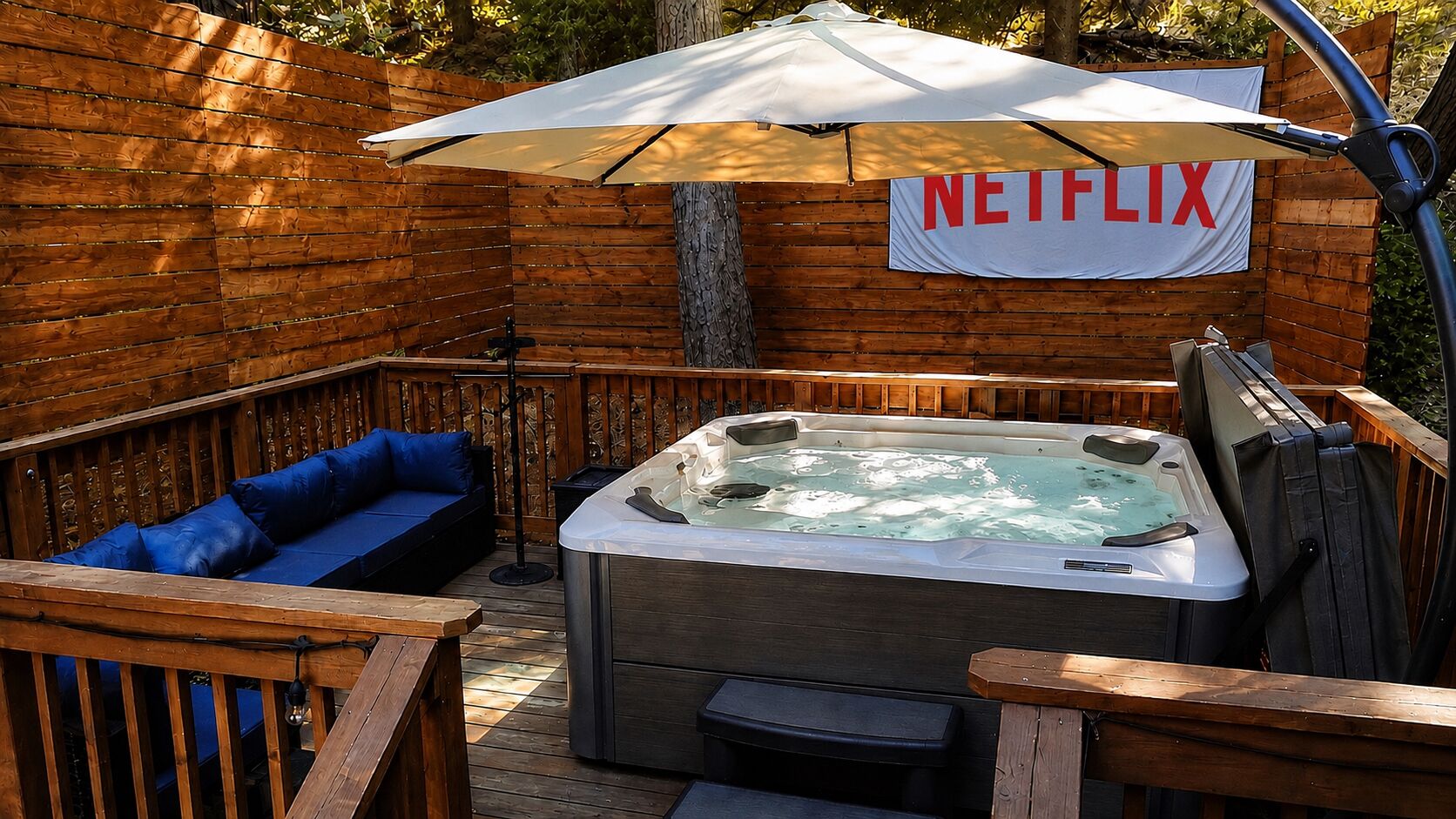A wooden deck with a hot tub, a blue sofa, and an umbrella.
