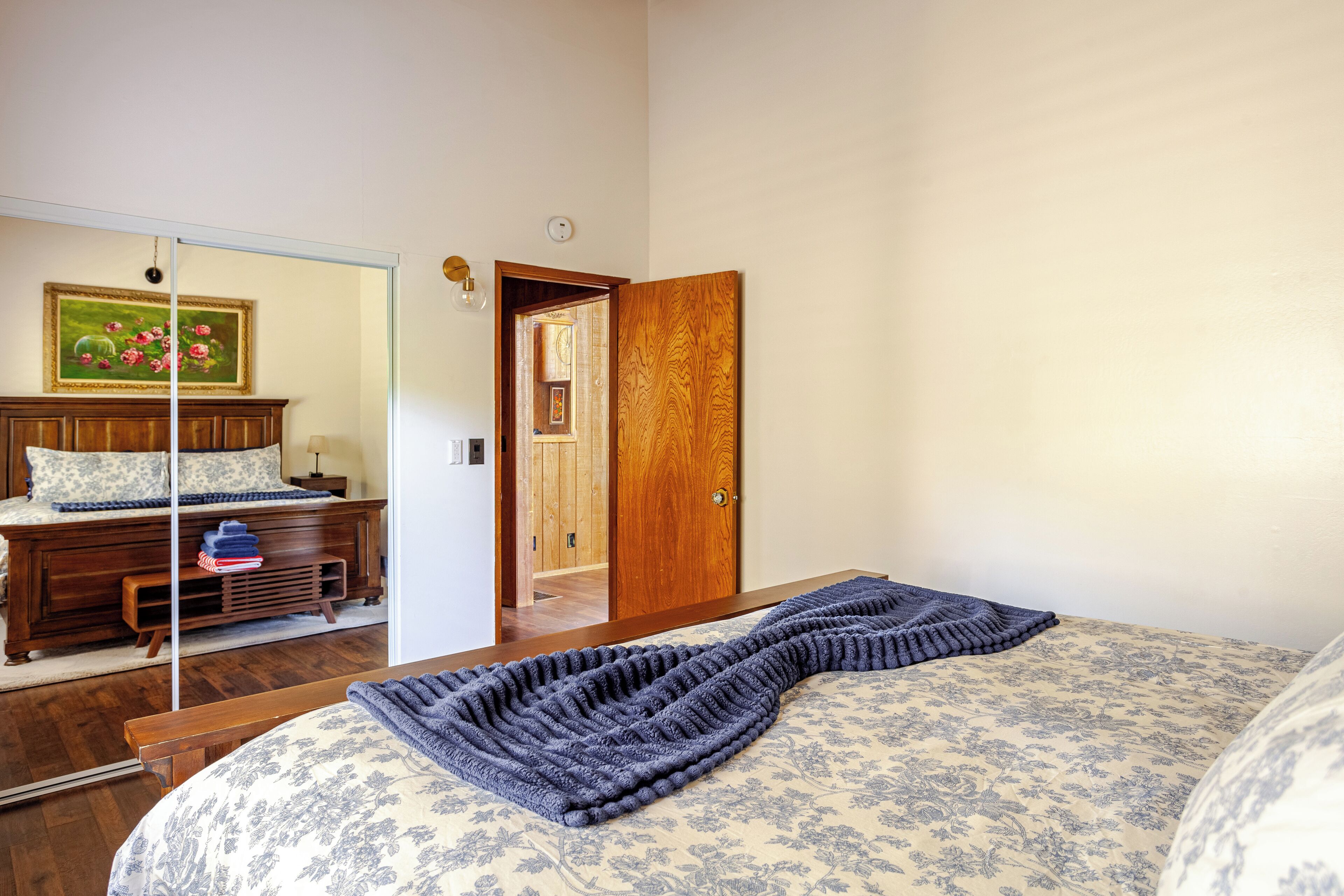 Un dormitorio con cama, cómoda de madera, espejo y puerta que da a otra habitación.