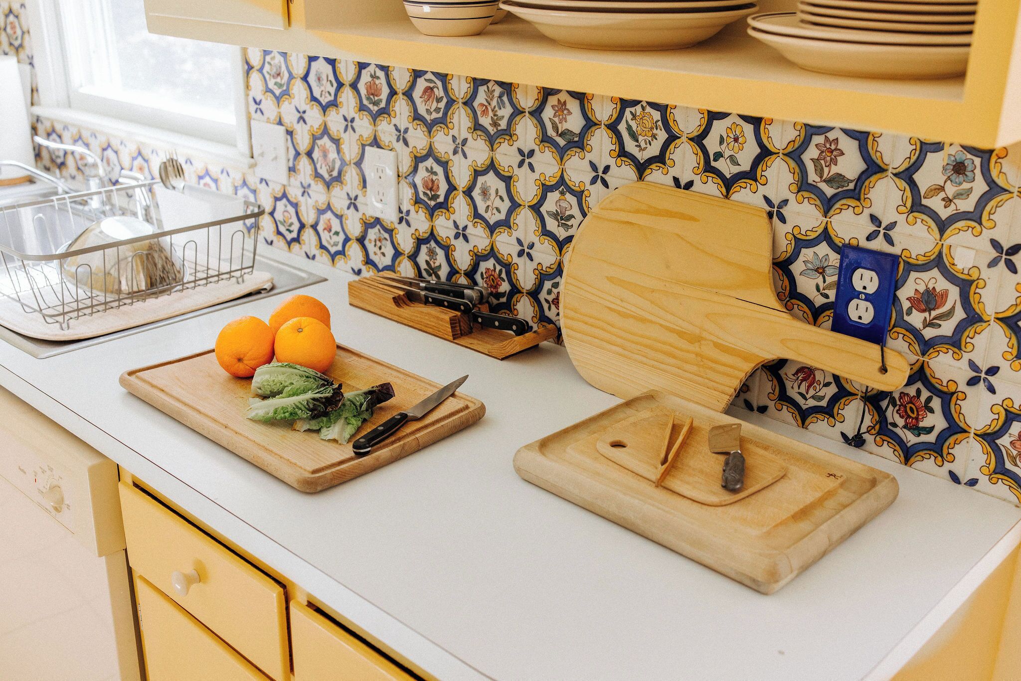 A kitchen with a white countertop, a wooden cutting board with vegetables, and a knife.