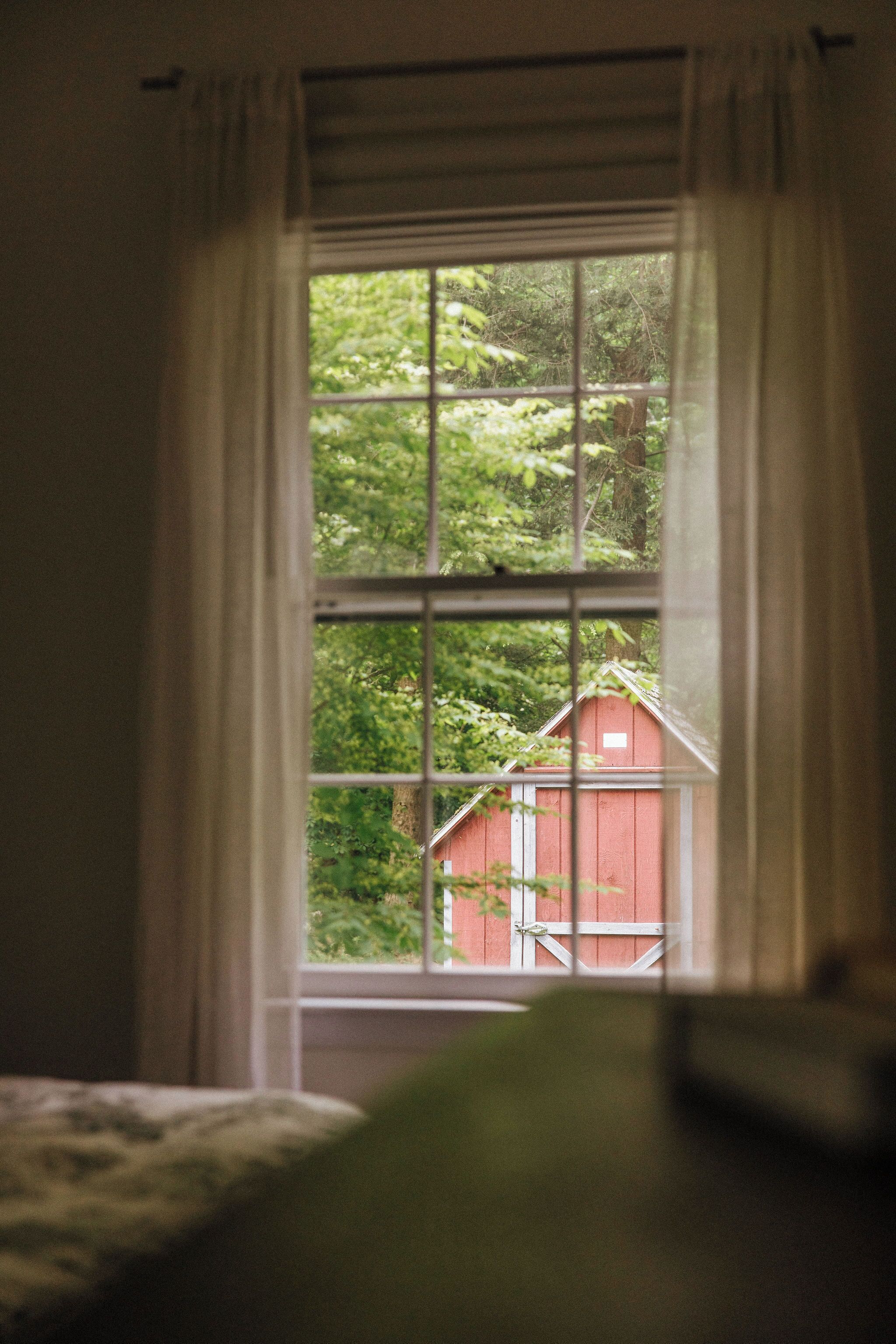 Ein Zimmer mit Blick auf eine rote Scheune und viel Grün.