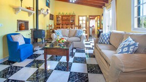 Amplia sala de estar con piso a cuadros, un sillón azul, un sofá color beige y una mesa de centro de madera.