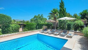 Piscina con sillas de descanso y sombrillas, rodeada de vegetación y un cielo despejado.