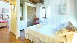 Un dormitorio con pared de piedra, cama con dosel, mesita de noche, una silla y ventana con cortinas.