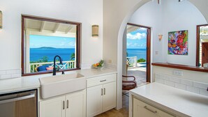 A kitchen with a view of the ocean, a sink, cabinets, and a countertop.