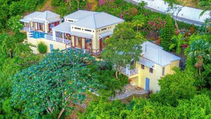 A cluster of three two-story houses with blue roofs and white railings, surrounded by lush greenery and flowering plants.