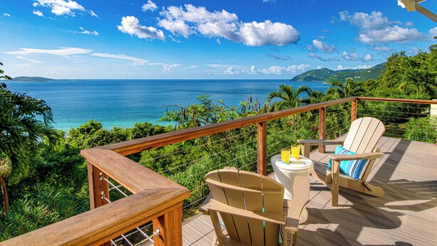 A wooden deck with a view of the ocean, a chair, a table, and a drink.