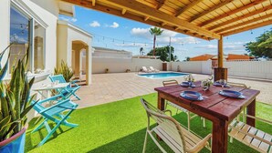 Un patio couvert avec une piscine, des sièges d’extérieur et un espace repas.
