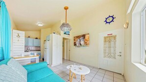 Un salon comprenant un canapé, une table à manger avec des chaises, un coin cuisine et une porte ornée d’un panneau de verre décoratif.