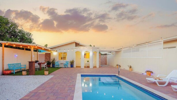 Un jardin avec une piscine, un espace salon extérieur et une terrasse couverte.