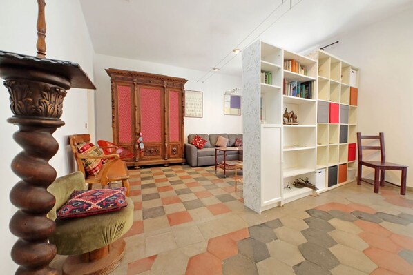 Un salon avec un sol à carreaux, une chaise en bois avec un coussin, un canapé avec des oreillers, une bibliothèque et un meuble en bois.