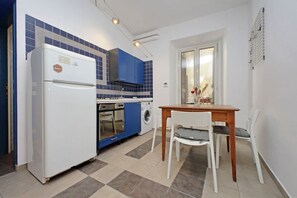 Une cuisine compacte équipée d’un réfrigérateur, d’un four et d’un lave-linge, une table à manger avec des chaises et une fenêtre donnant sur un paysage agréable.