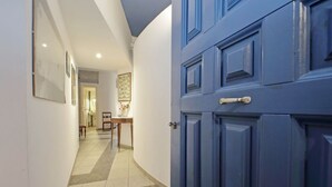 Un couloir avec une porte bleue, un sol carrelé et, au fond, un coin repas.