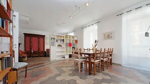 Une pièce dotée d’un sol à motifs hexagonaux, d’une table à manger avec des chaises, d’une bibliothèque et d’une grande fenêtre ornée de rideaux légers.