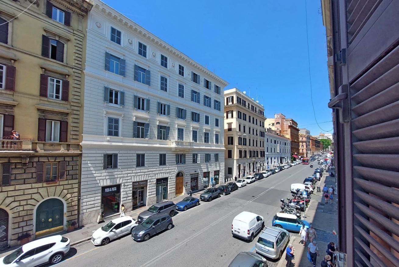A street view with multi-story buildings, parked cars, and a clear sky.