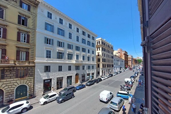 A street view with multi-story buildings, parked cars, and a clear sky.