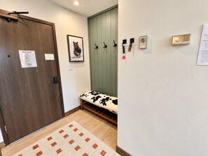 Un pasillo con una puerta de madera, un banco con cojín estampado de vaca, un aviso en la puerta e interruptor de luz en la pared.