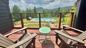 Una terrassa de fusta amb dues cadires Adirondack i una taula petita, amb vista a una piscina i un paisatge verd.